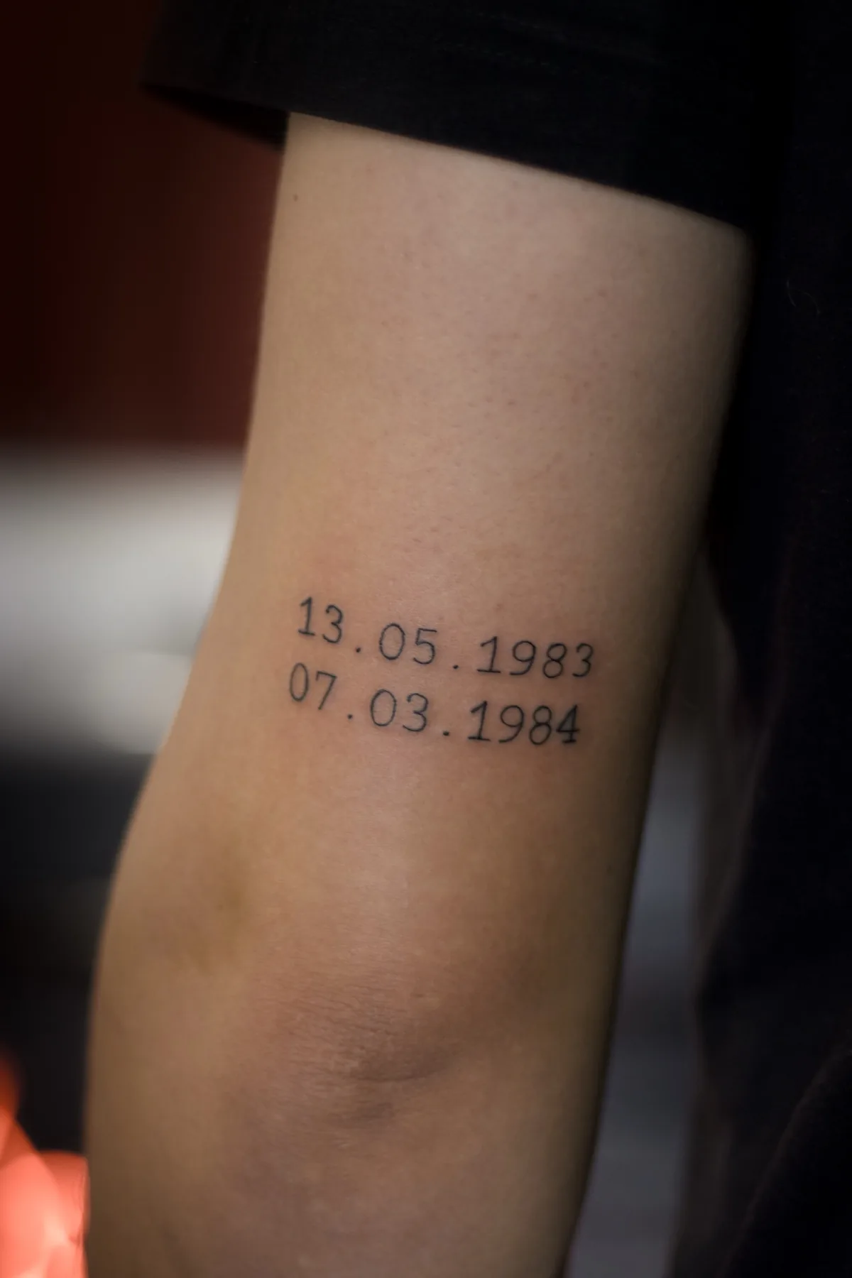 Minimalist fine line tattoo of two dates in typewriter-style lettering on the inner upper arm, Prague by Andrey Kovalov