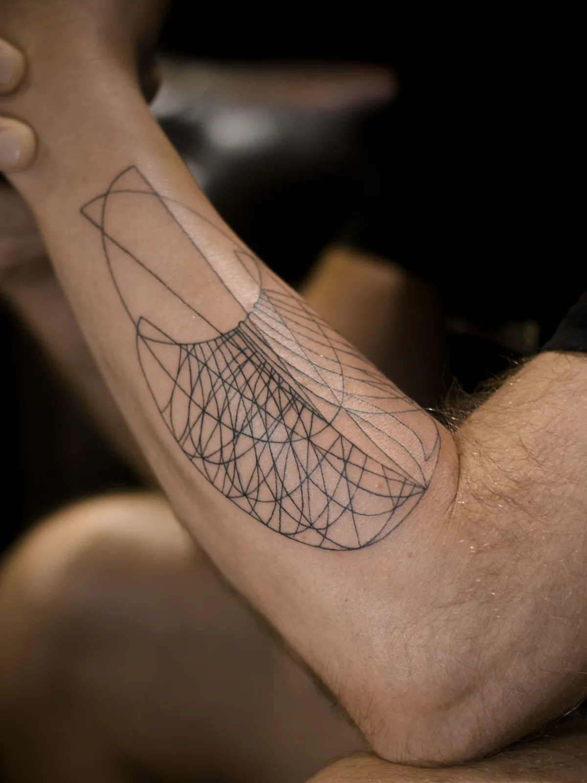 Abstract parametric linework tattoo wrapping the inner forearm and elbow with layered geometric curves, Prague by Andrey Kovalov